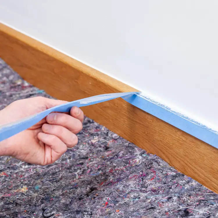 Ręka usuwa niebieską taśmę malarską Tesa Washi UV 2w1 po zakończeniu malowania ściany
