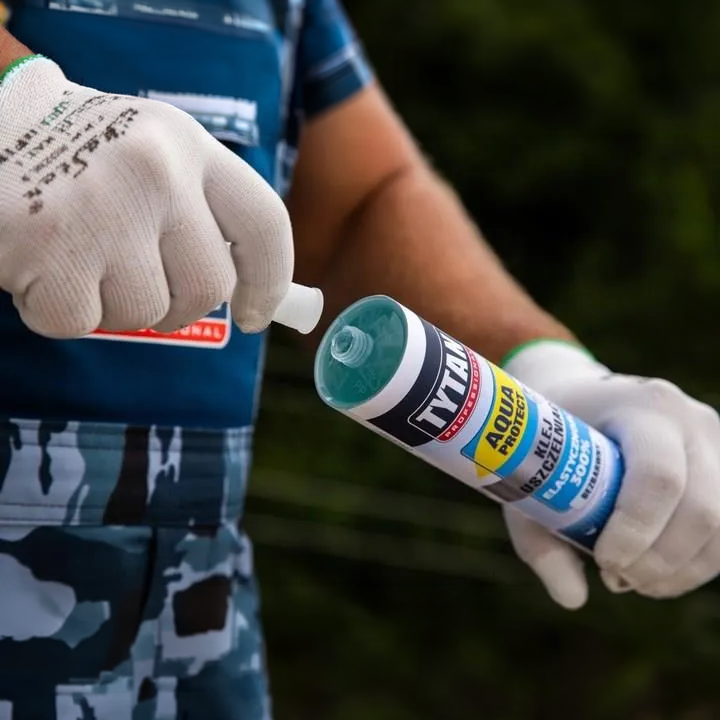 Ręka w rękawicy ściska tubę Tytan Aqua Protect podczas aplikacji na zewnątrz