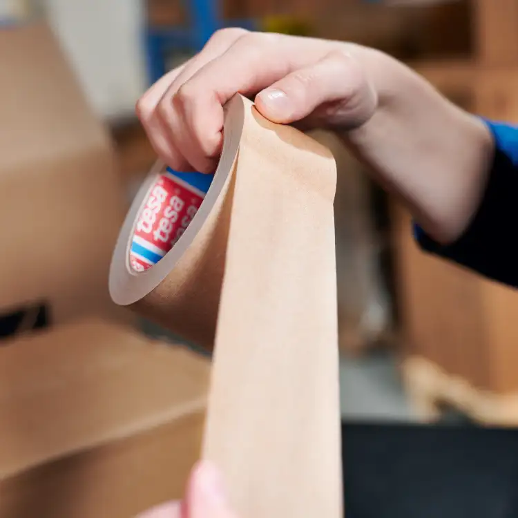 Rolka papierowej taśmy Tesa rozwijana ręcznie podczas przygotowywania paczki do wysyłki w magazynie
