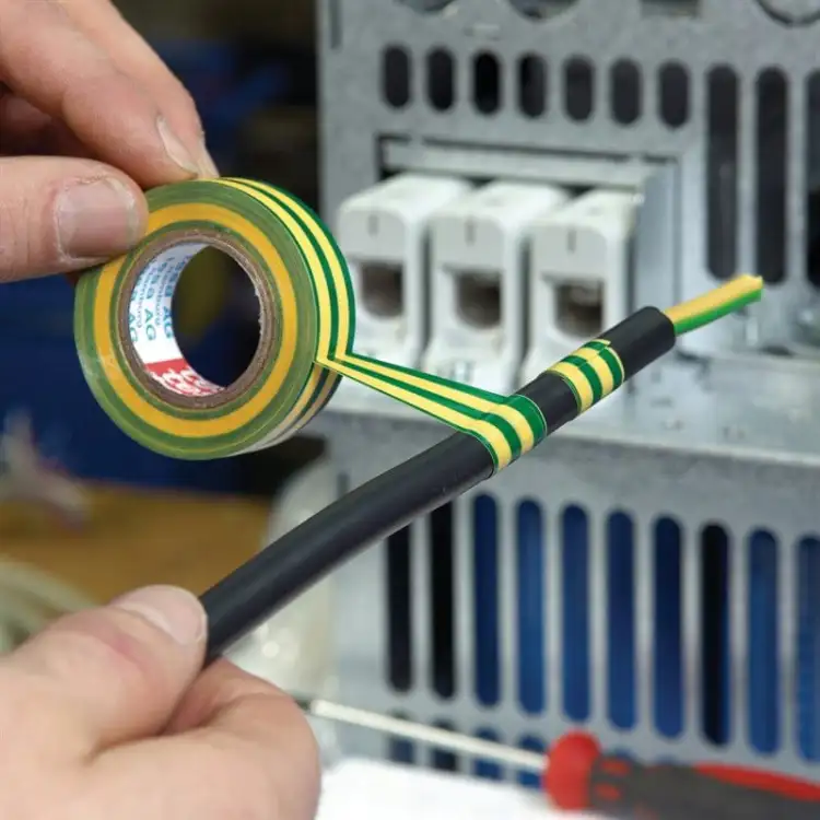 Osoba owija przewód czarną taśmą Tesa podczas prac przy instalacji elektrycznej