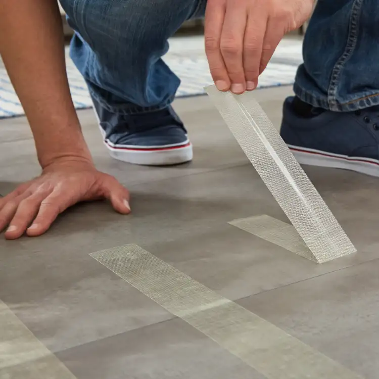 Mężczyzna przykleja dwustronną taśmę montażową Tesa na jasnej podłodze przed ułożeniem wykładziny