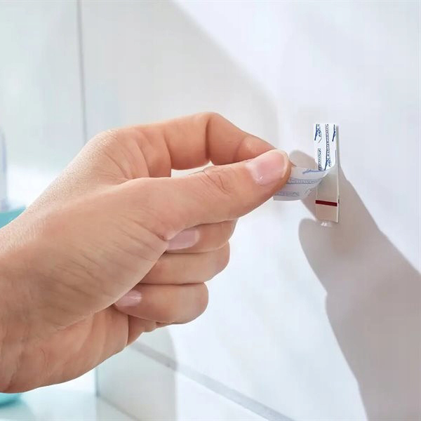 Dłoń dociska haczyk samoprzylepny Tesa Powerstrips do białych łazienkowych płytek ściennych
