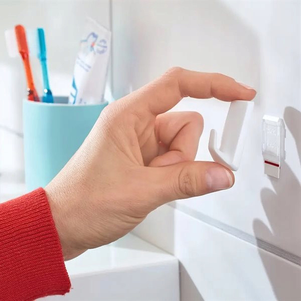 Palce trzymają haczyk Tesa Powerstrips przygotowany do zamocowania na białych płytkach łazienkowych