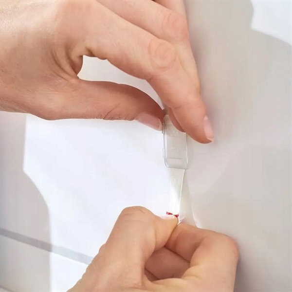 Dłoń odkleja pasek mocujący Tesa Powerstrips z białej płytki podczas demontażu haczyka łazienkowego