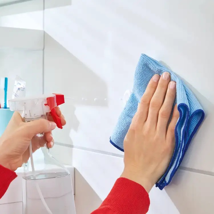 Ręka czyści płytki łazienkowe przed montażem samoprzylepnych haczyków Tesa Powerstrips