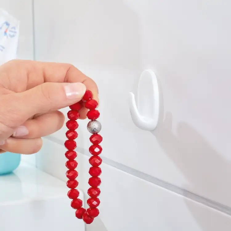 Czerwony koralikowy naszyjnik zawieszany na białym haczyku łazienkowym Tesa Powerstrips przyklejonym do ściany