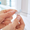 Osoba zbliża palce do samoprzylepnego haczyka łazienkowego Tesa Powerstrips podczas odklejania ochronnej warstwy