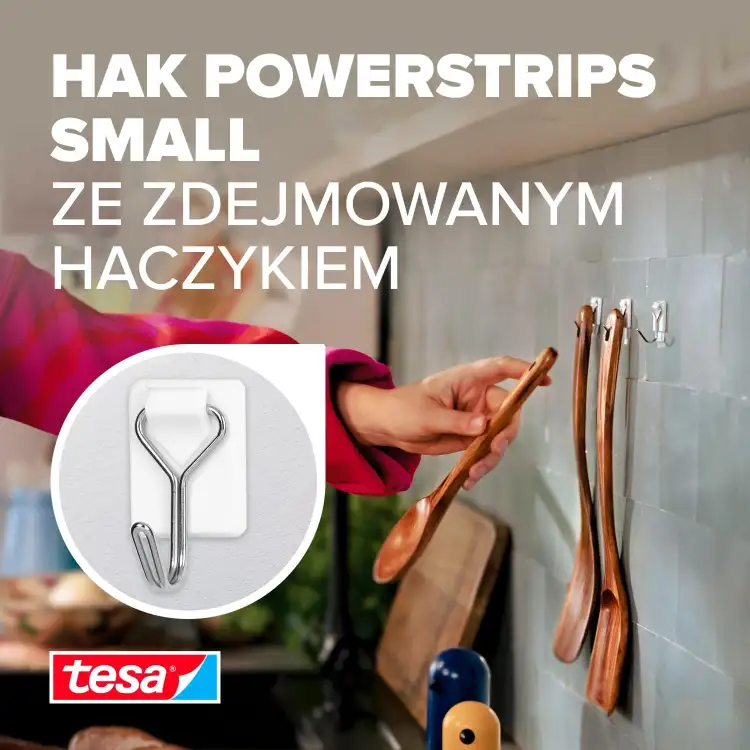 Na zdjęciu ręka zawiesza drewnianą łyżkę kuchenną na białym haczyku drucianym Tesa przy ścianie