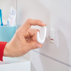 Montaż białego haczyka łazienkowego Tesa Powerstrips na czystych kafelkach obok niebieskiego pojemnika