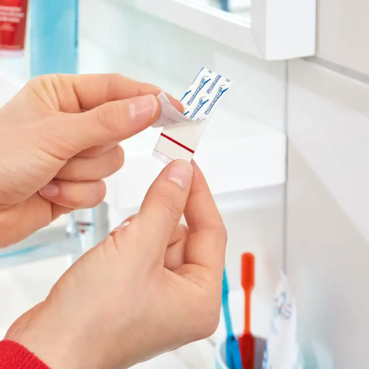 Osoba odkleja samoprzylepną taśmę montażową Tesa Powerstrips przygotowując ją do użycia w łazience