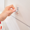Zbliżenie na montaż samoprzylepnego haczyka Tesa Powerstrips na białych płytkach łazienkowych