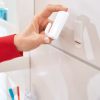 Ręka trzyma biały haczyk Tesa Powerstrips przed zamocowaniem na szafce w łazience