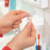 Osoba odkleja pasek samoprzylepny Tesa Powerstrips przygotowując haczyk łazienkowy do użycia
