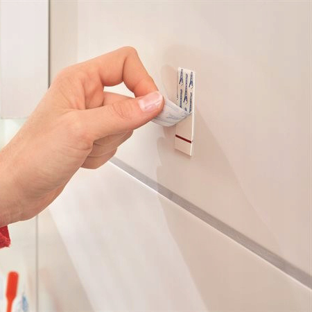 Ręka mocuje samoprzylepny haczyk łazienkowy Tesa Powerstrips na gładkiej powierzchni płytki