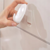 Zbliżenie na montaż biało-białego haczyka łazienkowego Tesa Powerstrips na ceramicznej ścianie