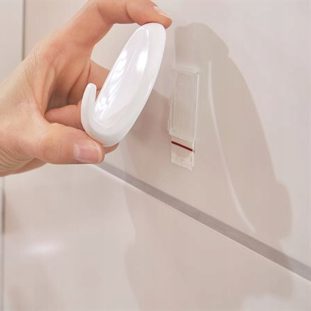 Zbliżenie na montaż biało-białego haczyka łazienkowego Tesa Powerstrips na ceramicznej ścianie