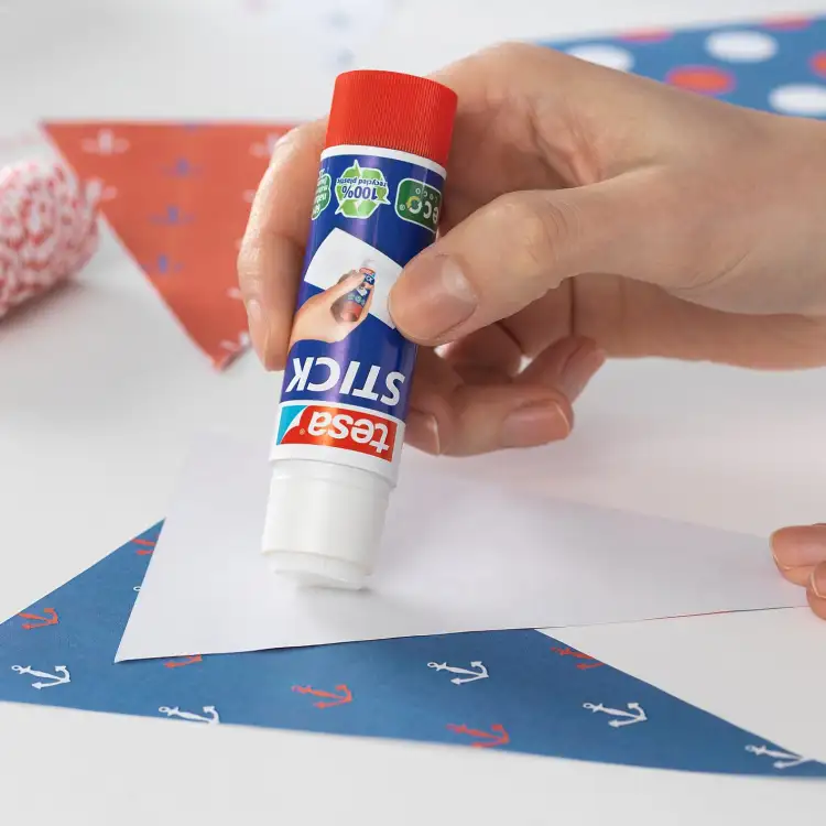 Ręka aplikuje klej Tesa Stick Glue na biały papier podczas tworzenia kolorowej dekoracji