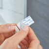 Osoba zbliża samoprzylepny haczyk Tesa Powerstrips do powierzchni, przygotowując go do montażu