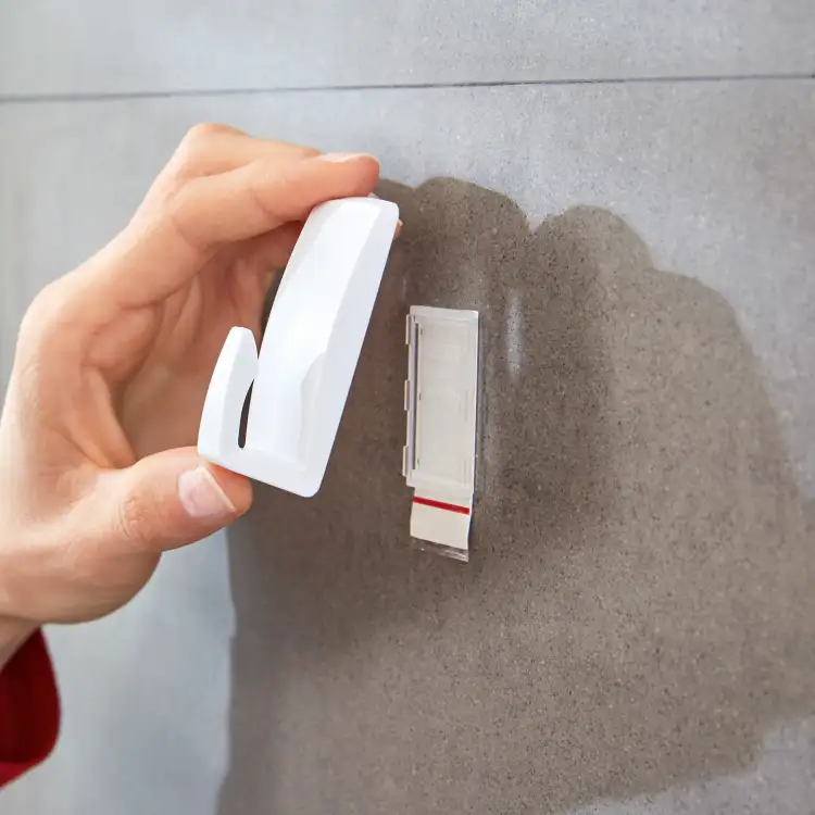 Biały haczyk łazienkowy Tesa Powerstrips gotowy do przyklejenia na gładkiej szarej płytce