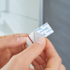 Osoba odkleja ochronną warstwę samoprzylepnej taśmy Tesa Powerstrips przed montażem w łazience
