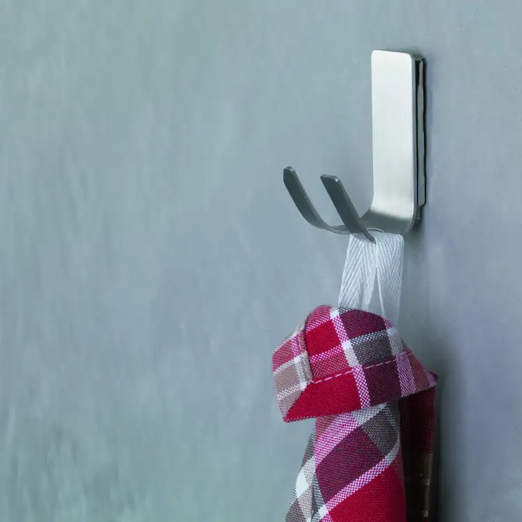 Na srebrnym metalowym haczyku łazienkowym Tesa Powerstrips wisi czerwona kraciasta ściereczka