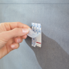 Palce odsłaniają warstwę ochronną samoprzylepnej taśmy Tesa Powerstrips na metalowym haczyku łazienkowym