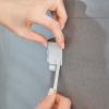 Ręka mocuje metalowy haczyk łazienkowy Tesa Powerstrips do szarej, gładkiej powierzchni ściany
