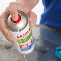 Ręka aplikuje preparat Tesa w sprayu na zabrudzoną powierzchnię metalowego blatu
