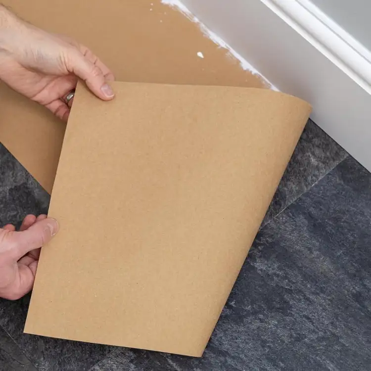 Brązowy papier ochronny Tesa samoprzylepny przyklejony wzdłuż ściany na ciemnej podłodze przed malowaniem