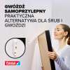 Kobieta montuje obraz na ścianie przy pomocy samoprzylepnego gwoździa Tesa do tapet