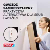 Kobieta montuje obraz na ścianie przy pomocy samoprzylepnego gwoździa Tesa do tapet