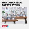 Na zdjęciu widoczne są różne opakowania produktów Tesa do mocowania na tapetach i tynku ustawione na stole