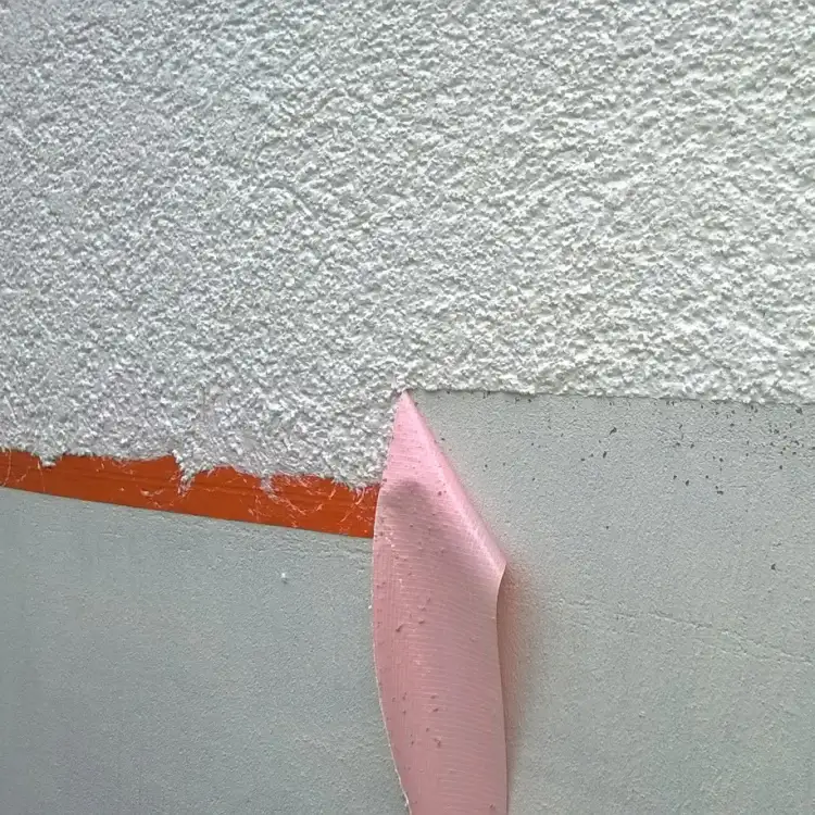 Pomarańczowa taśma Blue Dolphin widoczna podczas odcinania linii tynku na elewacji budynku