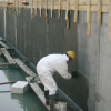 Pracownik nakłada mineralną powłokę hydroizolacyjną Ceresit CR 65 na betonową ścianę fundamentu