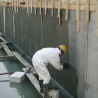 Pracownik nakłada mineralną powłokę hydroizolacyjną Ceresit CR 65 na betonową ścianę fundamentu