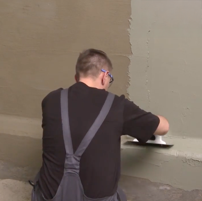 Mężczyzna nakłada mineralną izolację Ceresit CR 65 na ścianę w narożniku pomieszczenia
