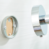Metalowy uchwyt półki łazienkowej Tesa SMOOZ zbliżany do zamocowanej na ścianie podstawy montażowej